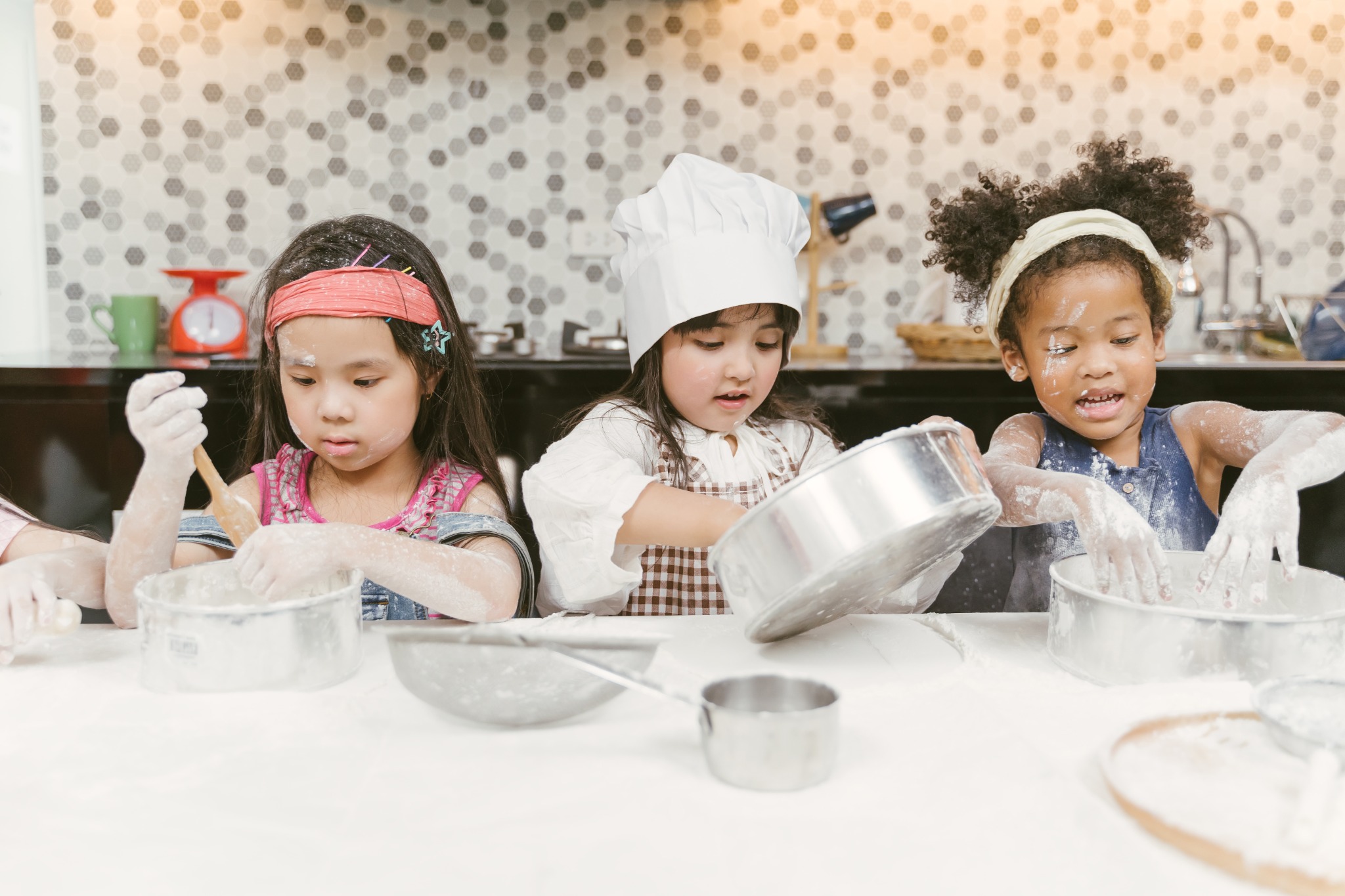 Three children in aprons mixing flour and baking together at a kitchen counter
