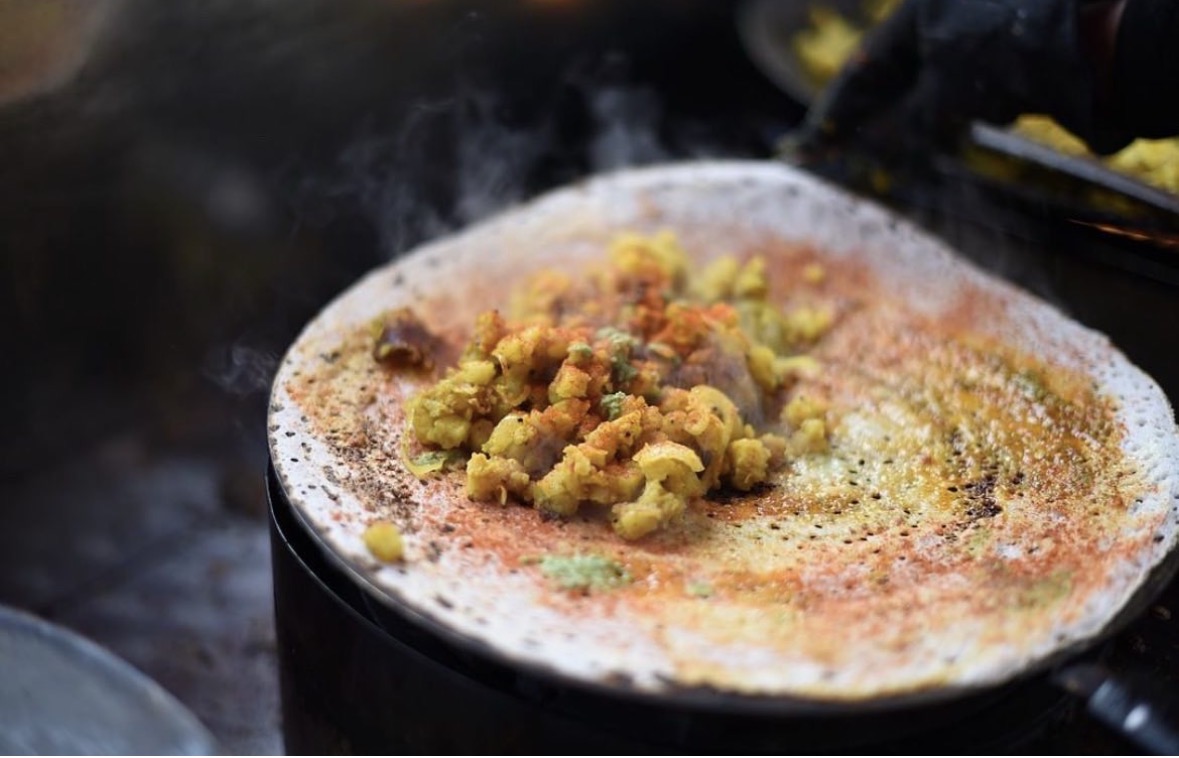 A dosa cooking on a hot tawa, topped with a spiced potato filling