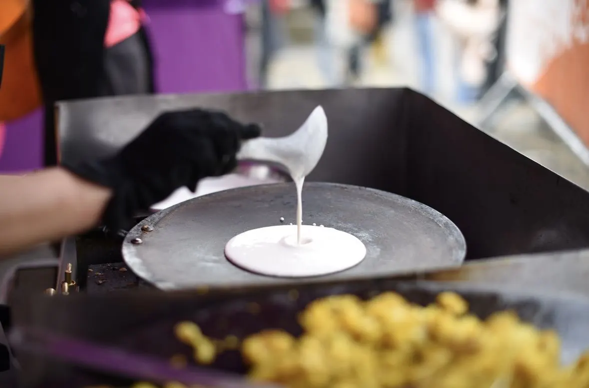 Fresh dosa batter being poured onto a hot griddle, forming a spiral